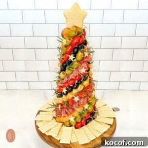 Decorated charcuterie tree standing vertically on a platter with a white background.