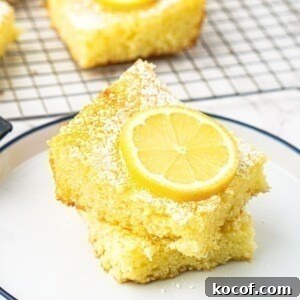 Bright yellow lemon bars stacked on a small white plate with a slice of lemon on top.