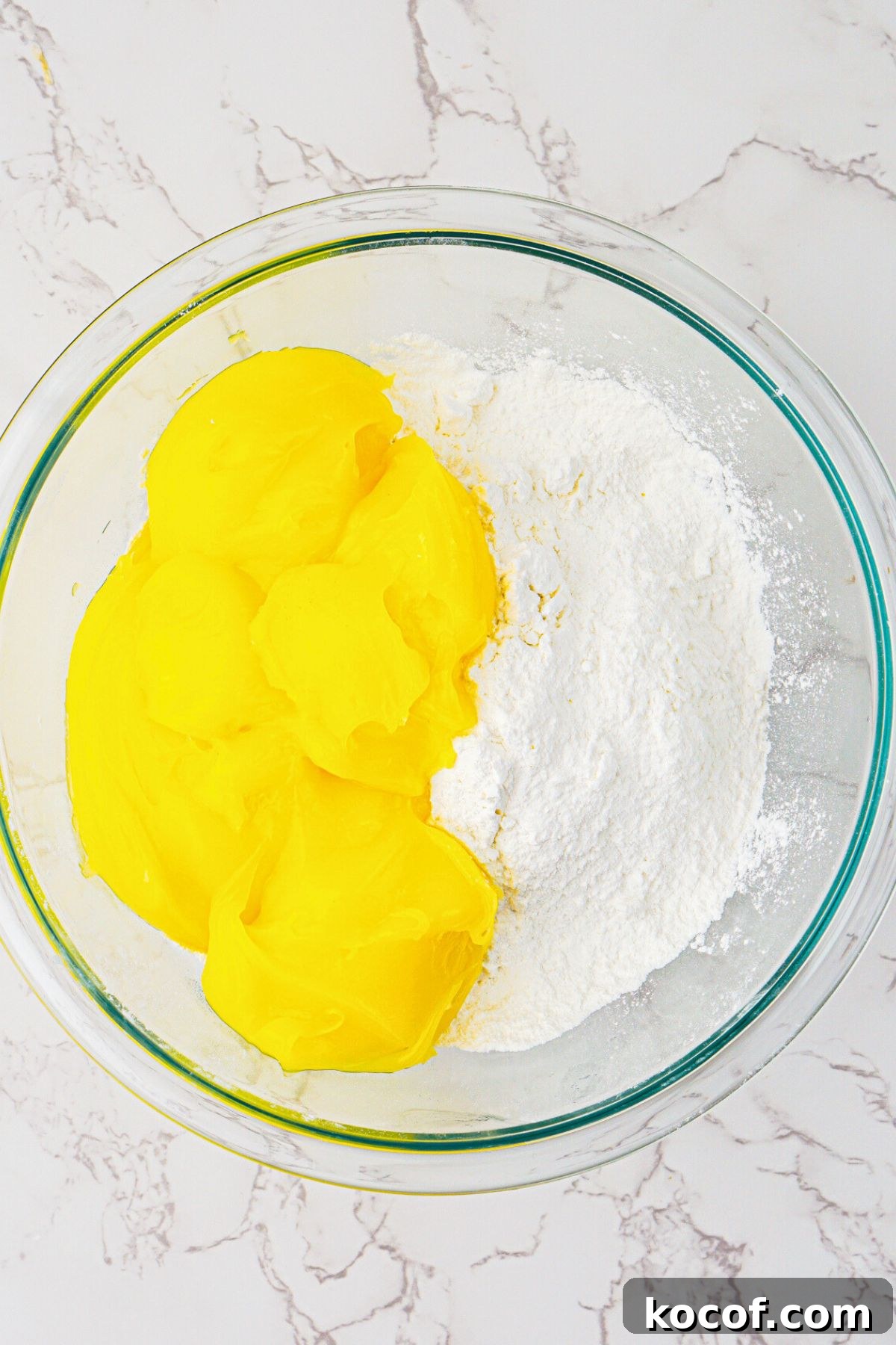 Cake mix and lemon pie filling being mixed together in a clear glass bowl. 