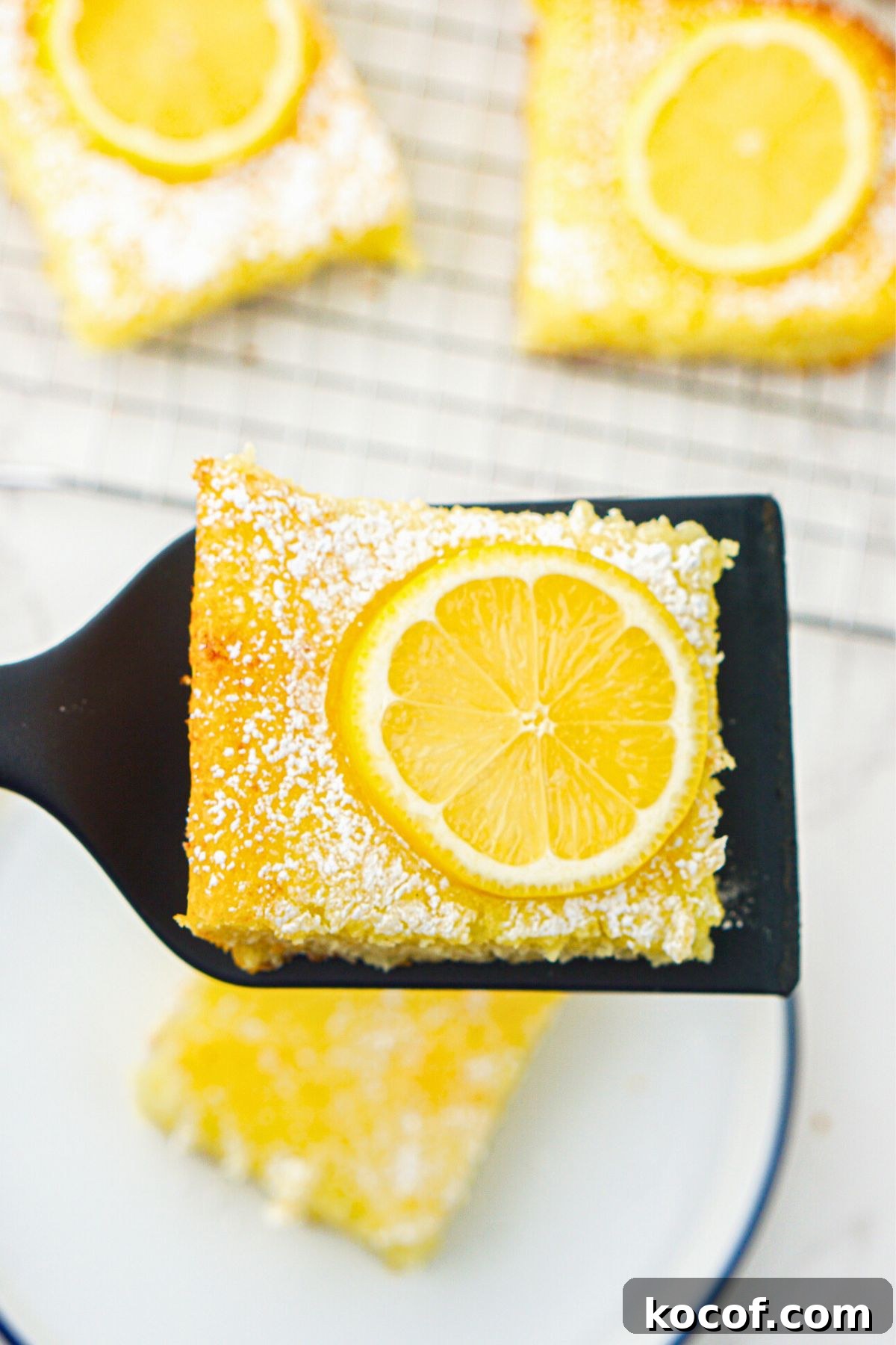 Bright yellow lemon bars after baking, with one being lifted to serve on a spatula. 