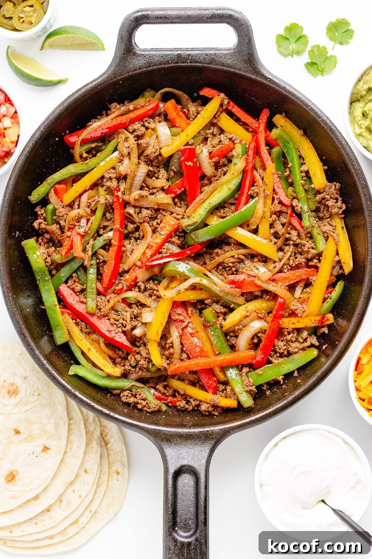 Quick Skillet Ground Beef Fajitas with Peppers and Onions 2 Ground beef and fajita veggie mixture in a cast iron skillet surrounded by tortillas and a variety of fajita toppings.