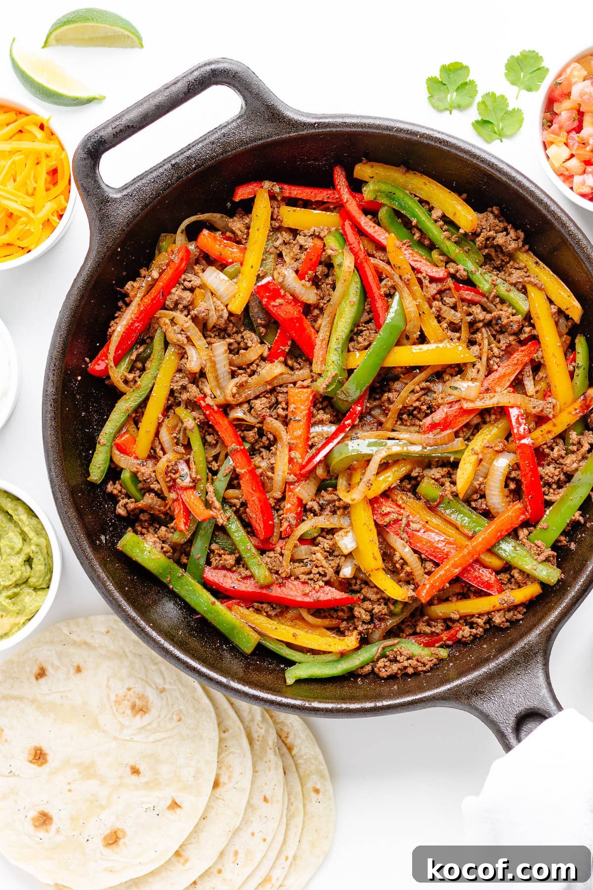 Quick Skillet Ground Beef Fajitas with Peppers and Onions 11 Cast iron skillet of ground beef fajitas mixture surrounded by tortillas and various toppings.