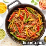 Ground beef fajitas mixture in a cast iron skillet surrounded by a variety of fajita toppings and tortillas.