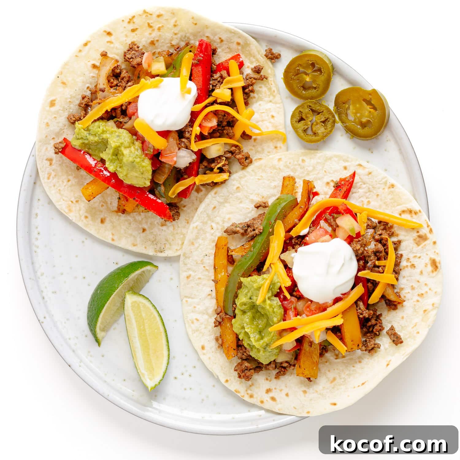 Quick Skillet Ground Beef Fajitas with Peppers and Onions 3 Two open ground beef fajitas on a plate with lime wedges and pickled jalapeno slices next to it.