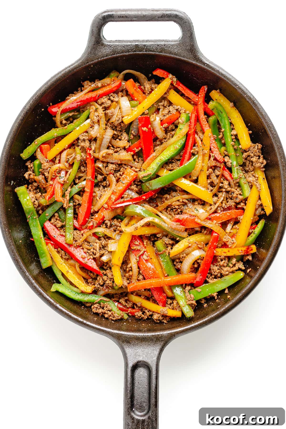 Quick Skillet Ground Beef Fajitas with Peppers and Onions 7 Seasoned ground beef and fajita veggies in a cast iron skillet on a white background.