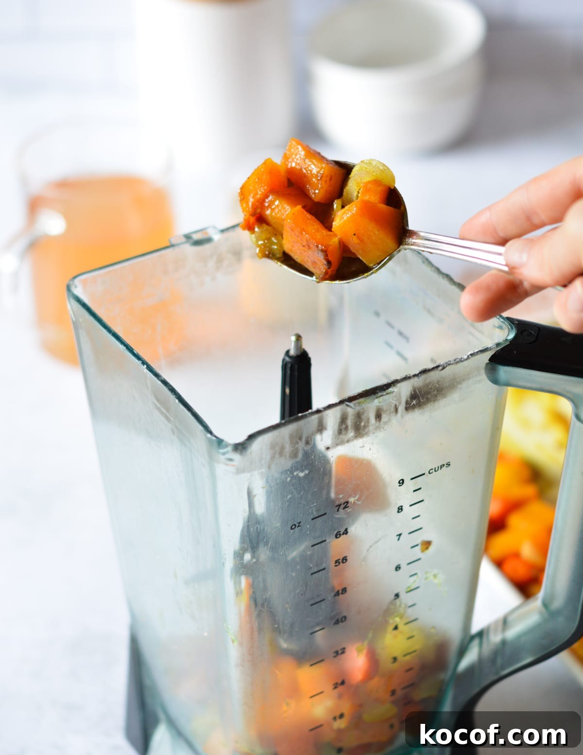 hand scooping roasted squash and dumping it into a blender. 