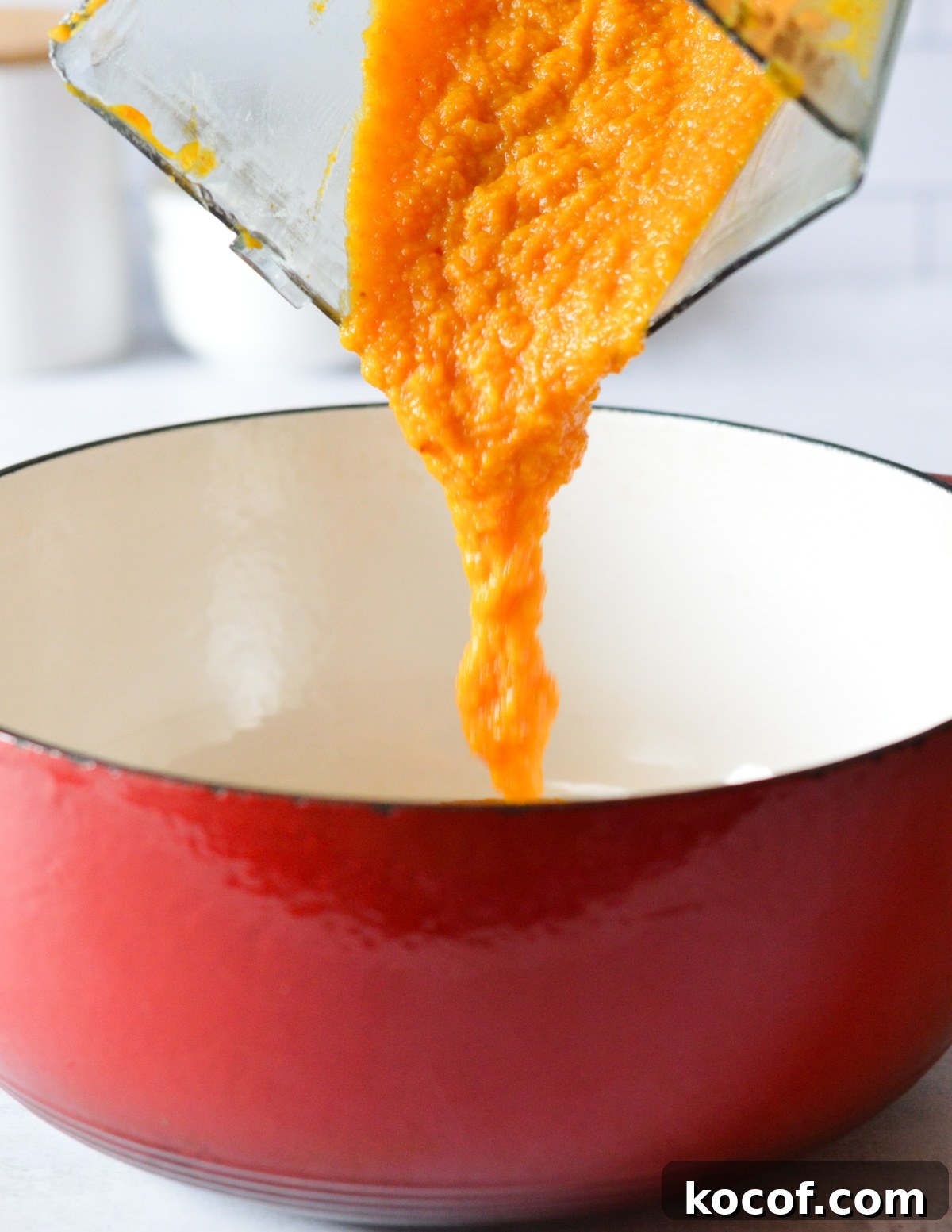 pouring butternut squash puree into a dutch oven pot. 