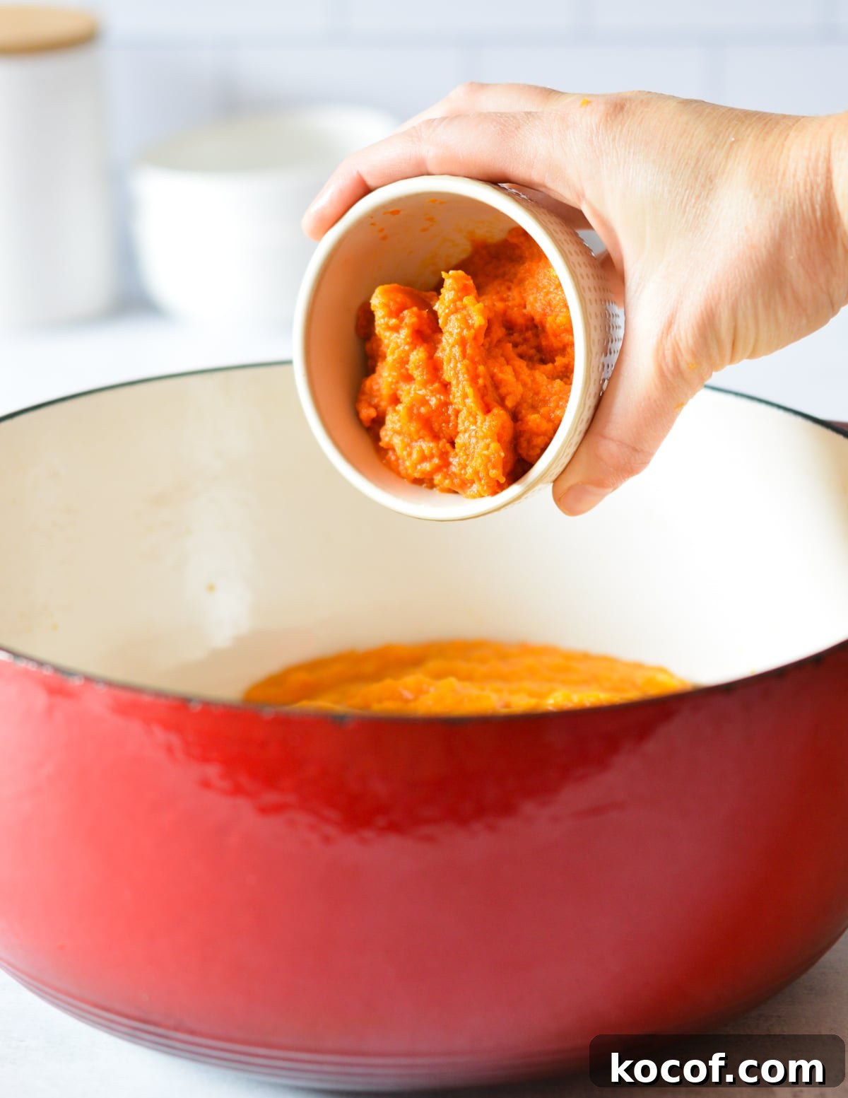 adding pumpkin puree to a large pot of butternut squash puree. 