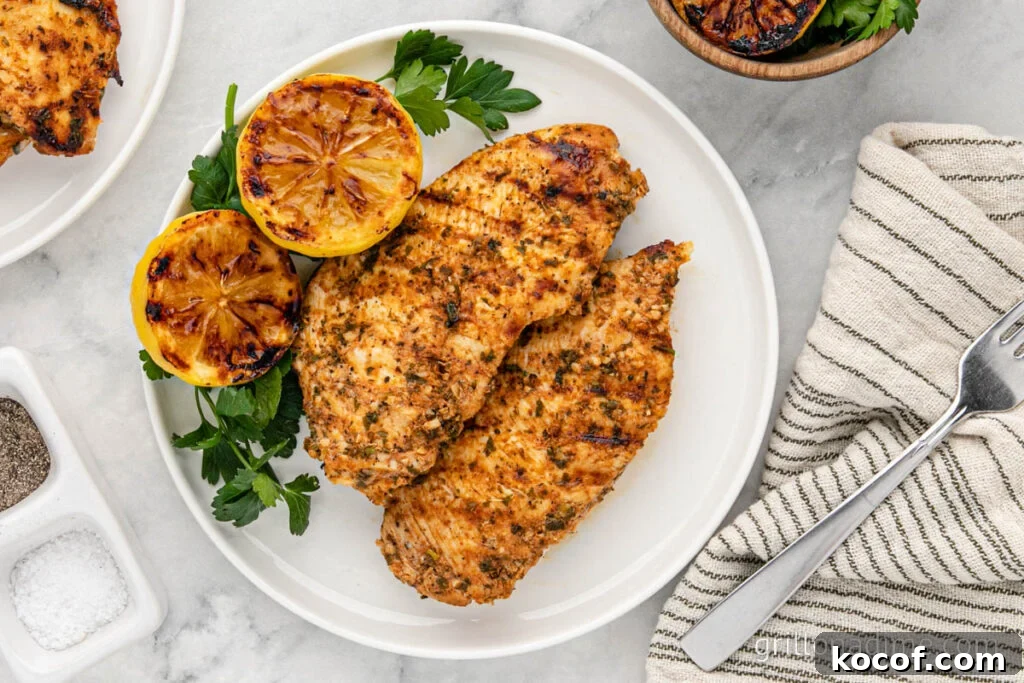 9 Juicy Grilled Chicken Recipes That Stay Moist Every Time 2 Juicy grilled lemon herb chicken breast with charred lemon halves and fresh parsley on white plate.