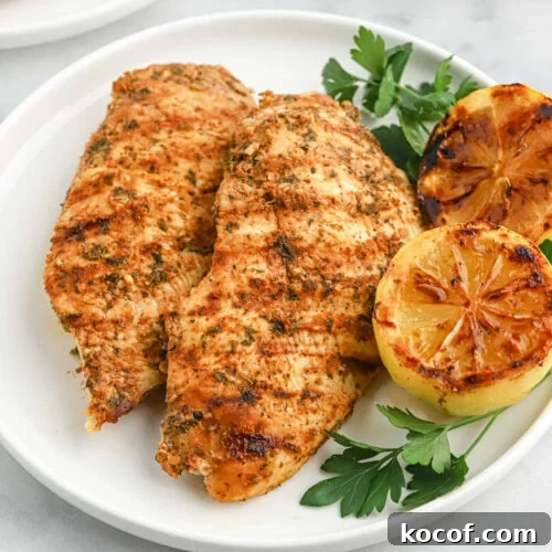 9 Juicy Grilled Chicken Recipes That Stay Moist Every Time 9 Juicy, seasoned grilled chicken breasts with roasted lemon halves and fresh herbs on a white plate.