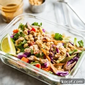 colorful thai chopped chicken salad in an individual serving glass meal prep container with peanut dressing + crushed peanuts in the background