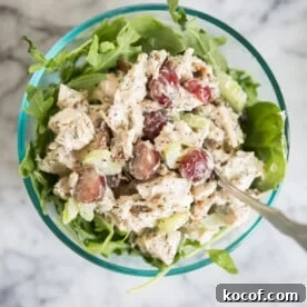 chicken salad with grapes and pecans over mixed greens in a glass bowl on a marble board