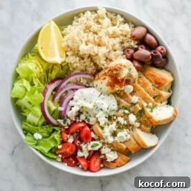 a green chicken power bowl made with brown rice, chicken, olives, cherry tomatoes, hummus, and lettuce