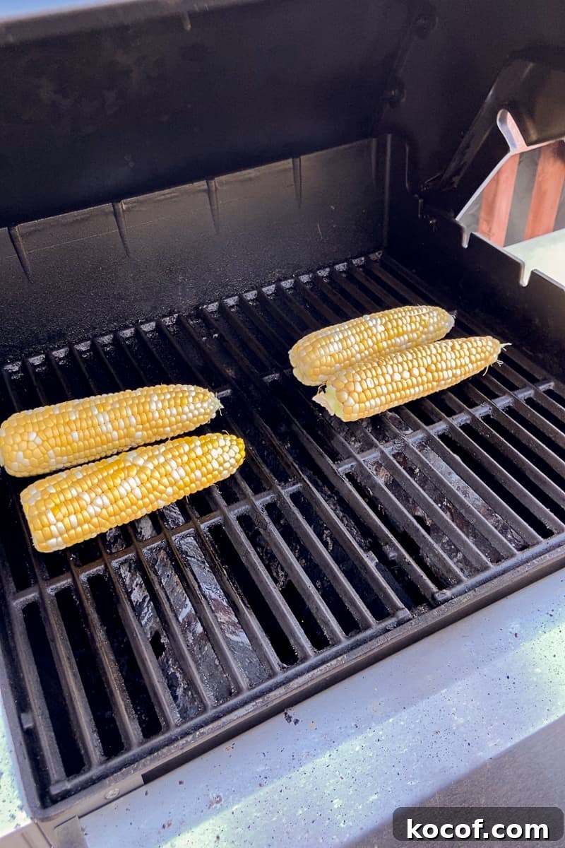 Four ears of corn are cooking on a grill, showing grill marks.