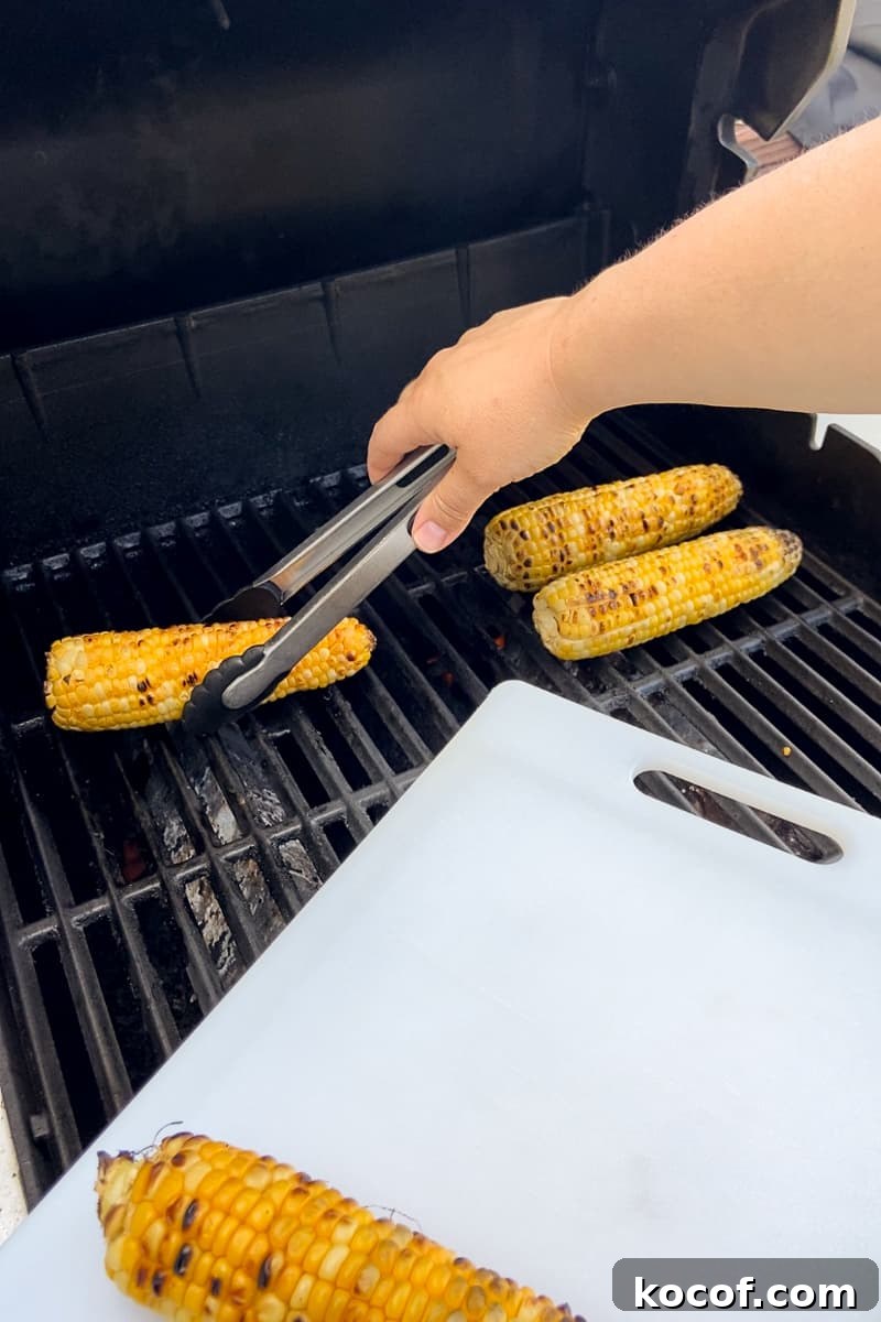 A person uses tongs to remove grilled corn on the cob from a barbecue grill.