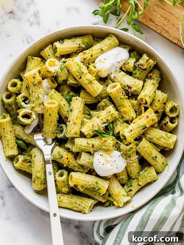 Bowl of pasta tossed with pea pesto and garnished with pea shoots, dollops of cream and cheese.