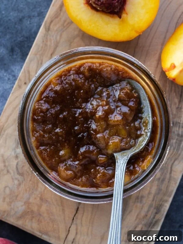 Maple peach chutney in a mason jar on a wooden board with fresh peaches on the side.