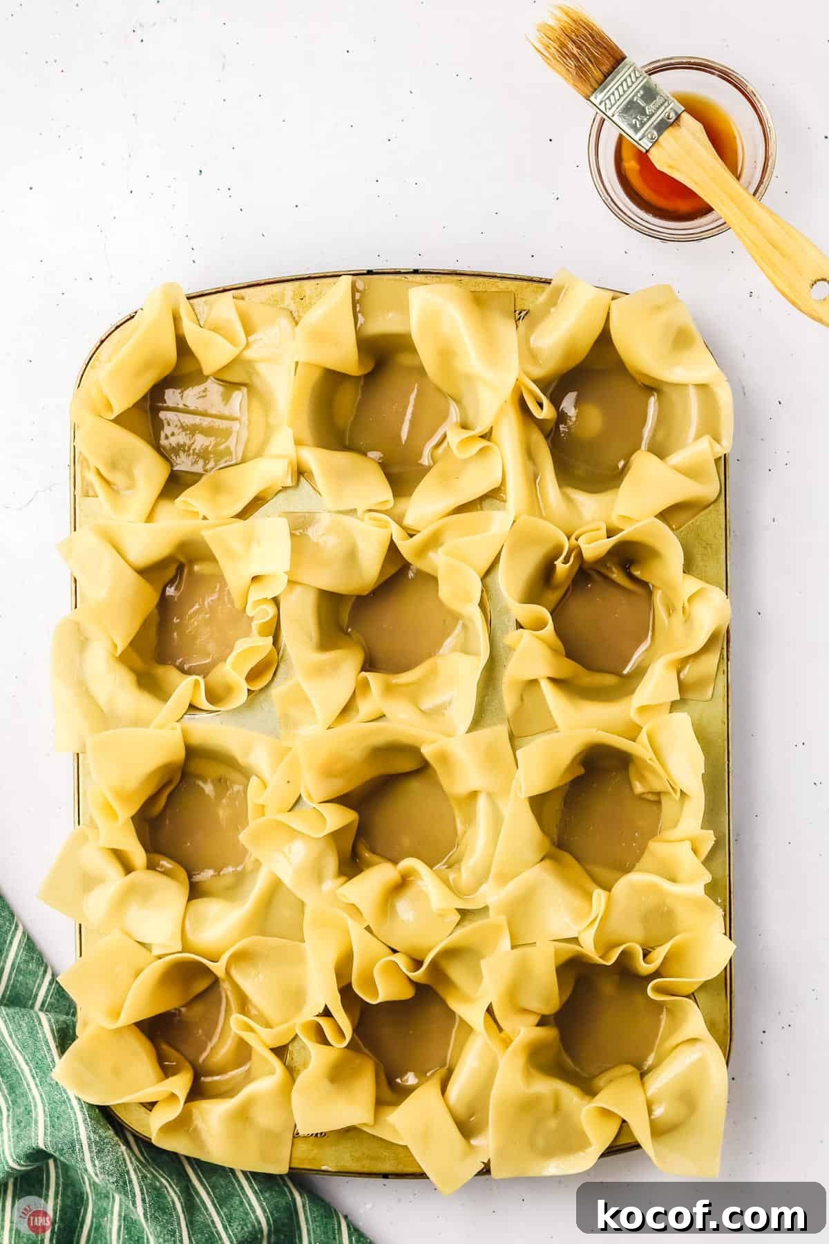 wonton wrappers being formed into cups in a muffin tin