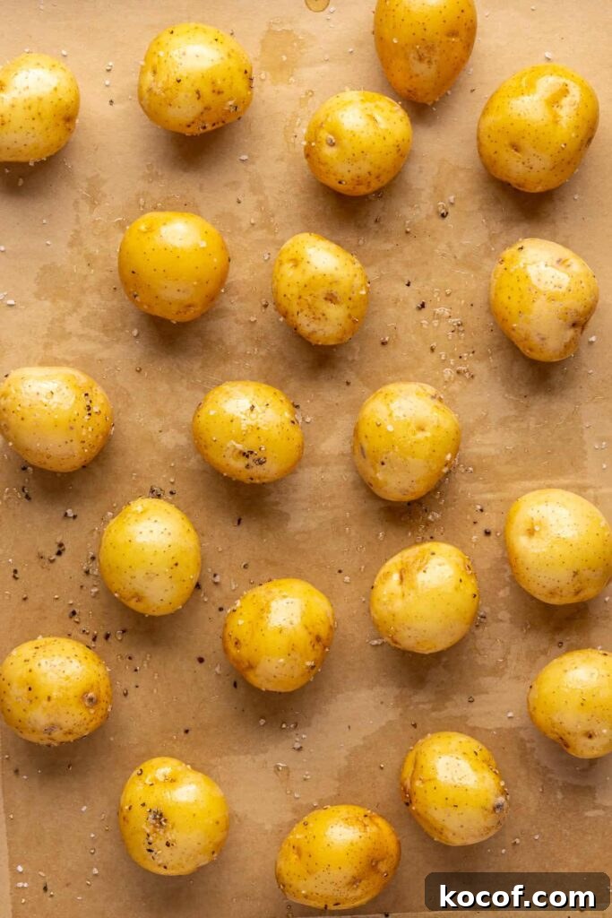 Mini Dutch potatoes coated in bacon grease and seasoning on a baking sheet