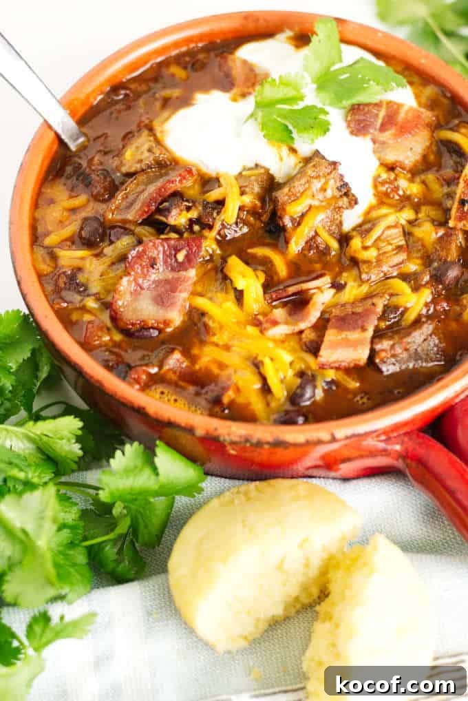 Smoked Brisket Chili Recipe: Bold, Smoky Chili with Beef Brisket 2 small red pot filled with brisket chili with cheese and sour cream and a garnish of cilantro, cornbread muffin in the foreground