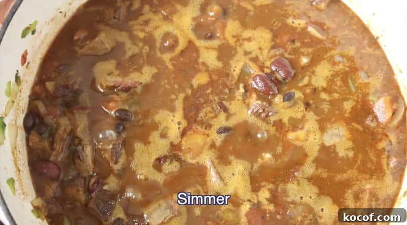 Smoked Brisket Chili Recipe: Bold, Smoky Chili with Beef Brisket 7 dutch oven filled with smoked brisket chili being simmered on low-medium heat burner
