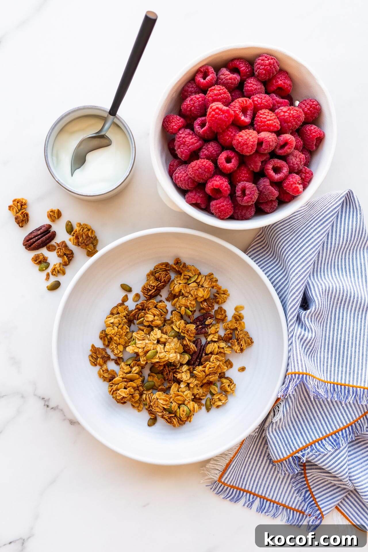 A bowl of granola clusters served with a bowl of berries and greek yogurt, striped linen napkin