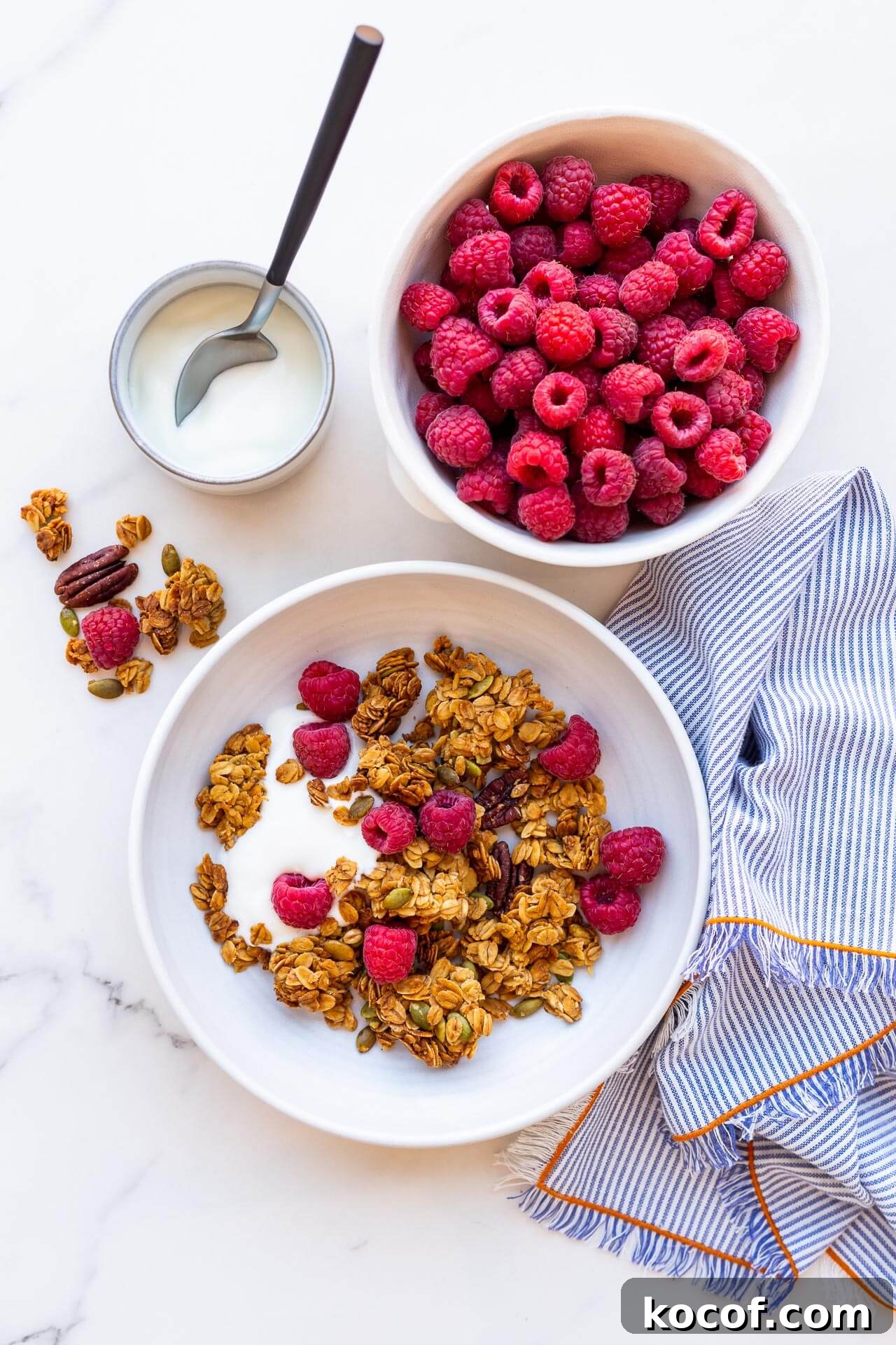 Bowl of granola clusters with yogurt and raspberries, striped linen napkin