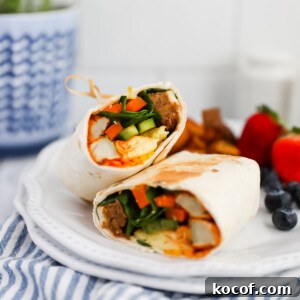 A breakfast burrito that has been sliced in half and is presented on a plate with fresh fruit.