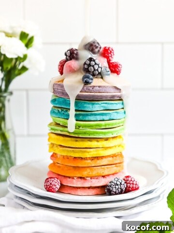 A stack of colorful pancakes with frozen fruit on top and a drizzle of white sugar sauce on top.