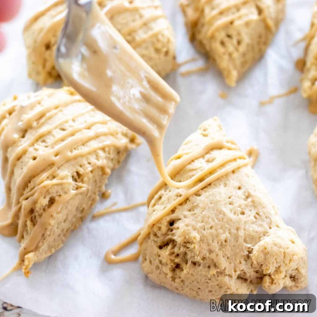 coffee scones on parchment being drizzled with glaze from a fork