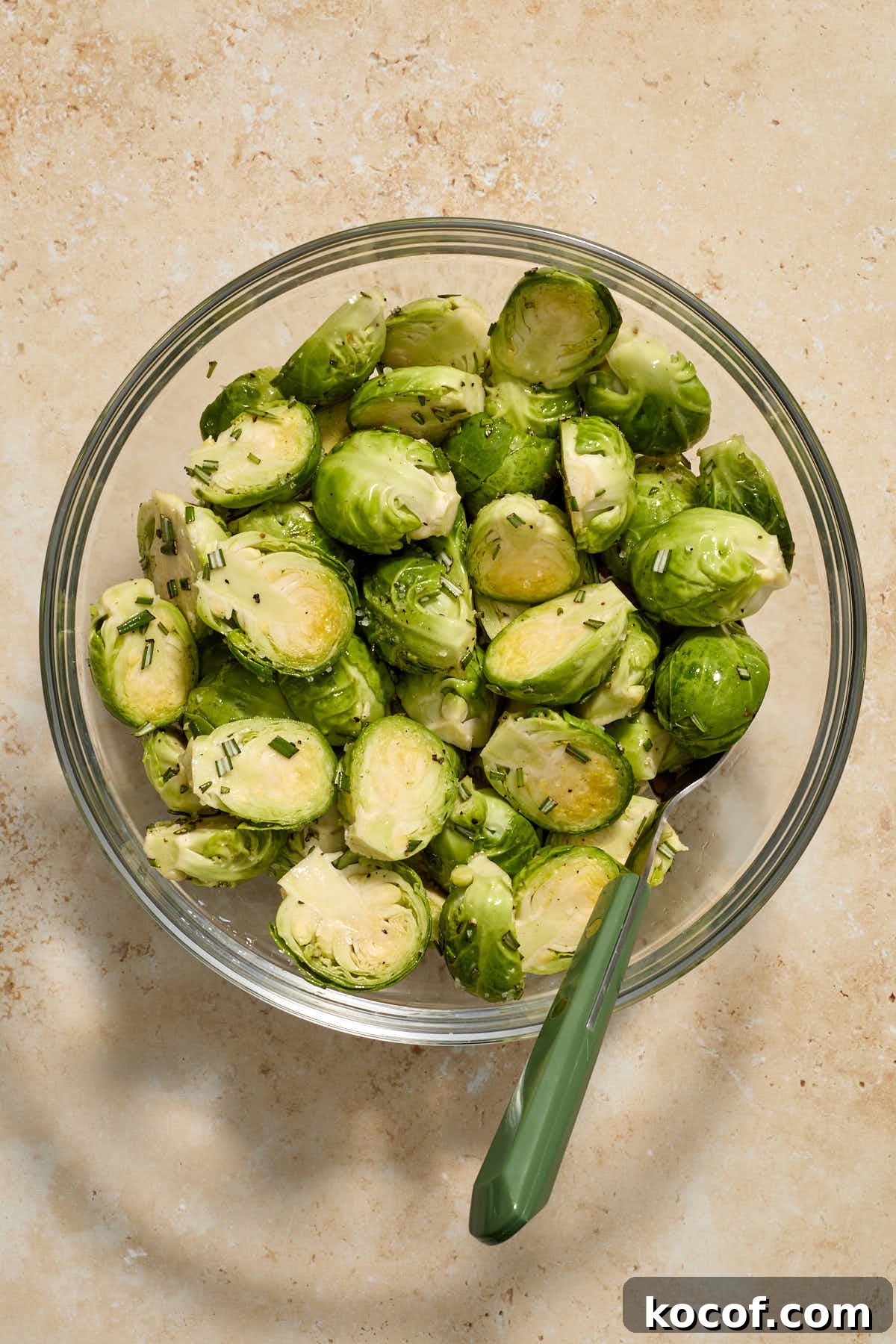 Trimmed and halved Brussels sprouts in a glass bowl and tossed with oil and seasonings.
