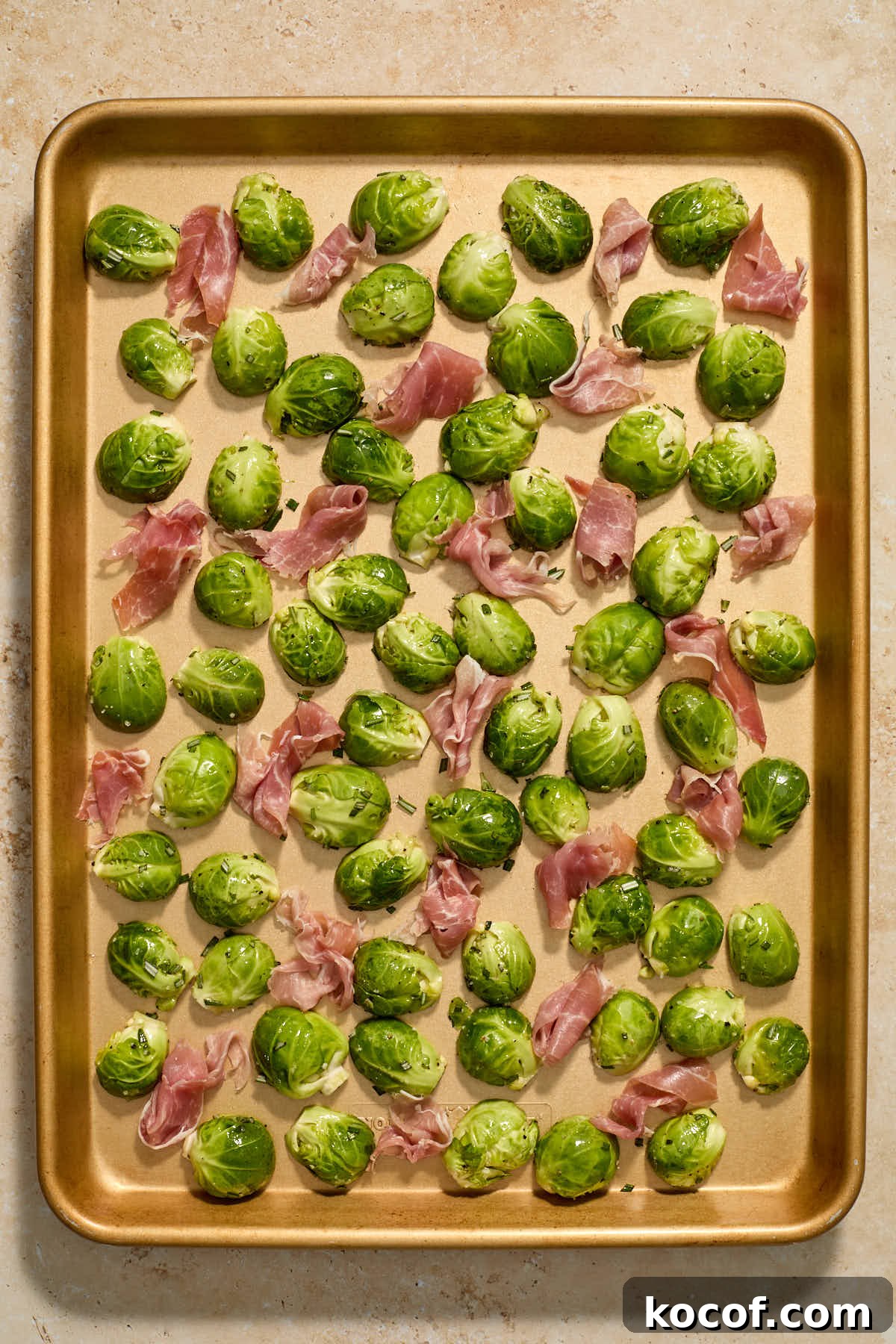 Torn pieces of prosciutto arranged around the Brussels sprouts on a sheet pan.