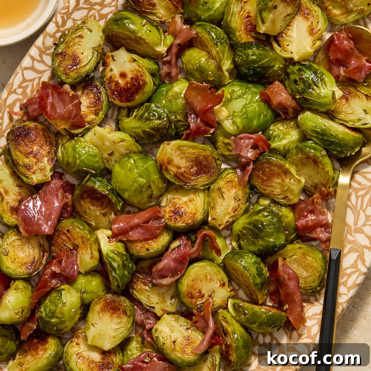 Roasted Brussels sprouts with prosciutto served on a platter with a serving spoon.
