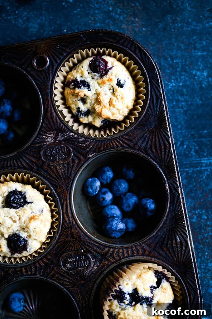 An overhead view of three Yogurt Blueberry Oatmeal Muffins and blueberries in a muffin tin.
