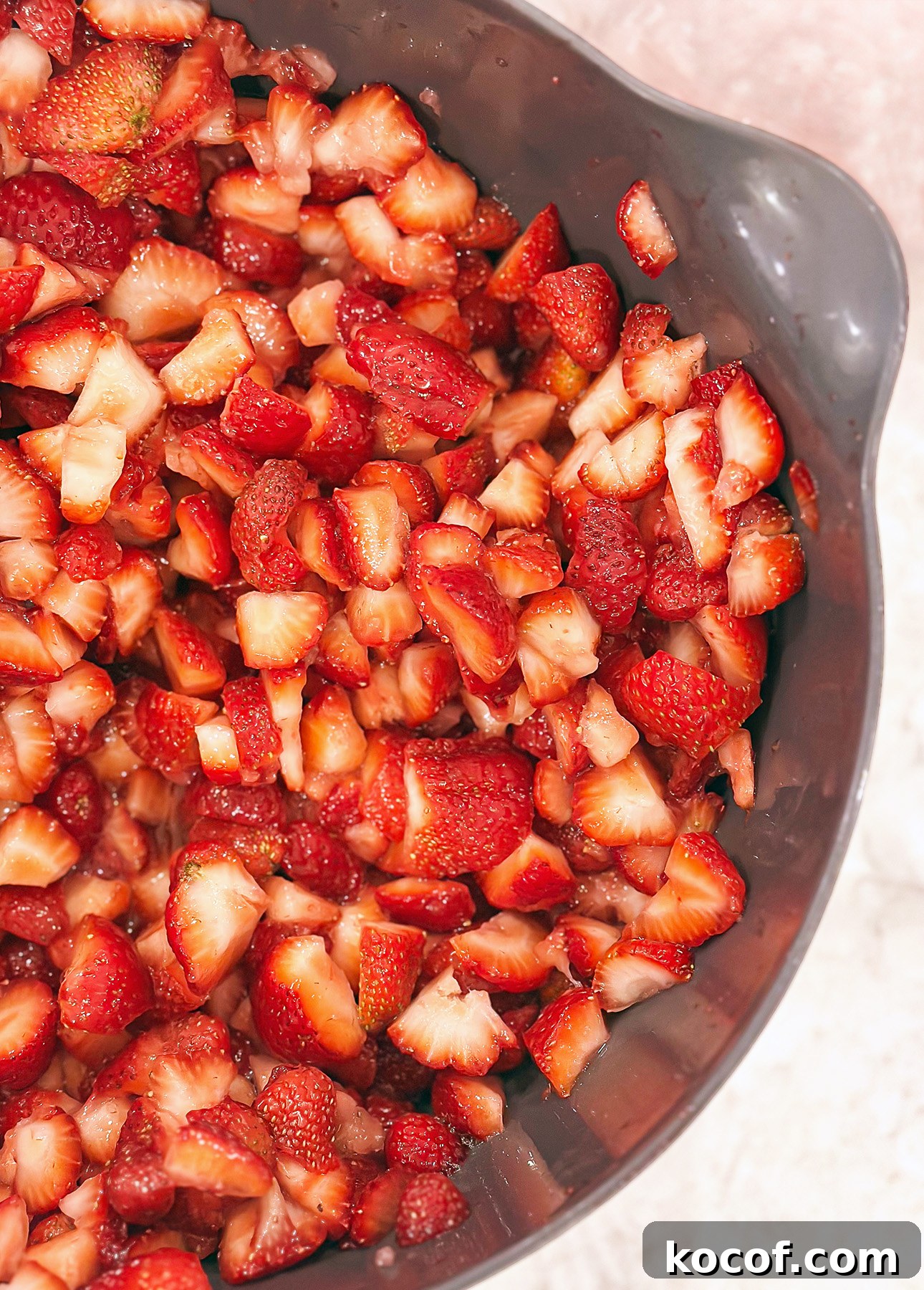 Lemon-Lime Citrus Mousse with Macerated Strawberries 5 A close-up of a gray bowl filled with freshly diced strawberries on a light-colored surface, perfect for topping a citrus mousse. // FoodNouveau.com