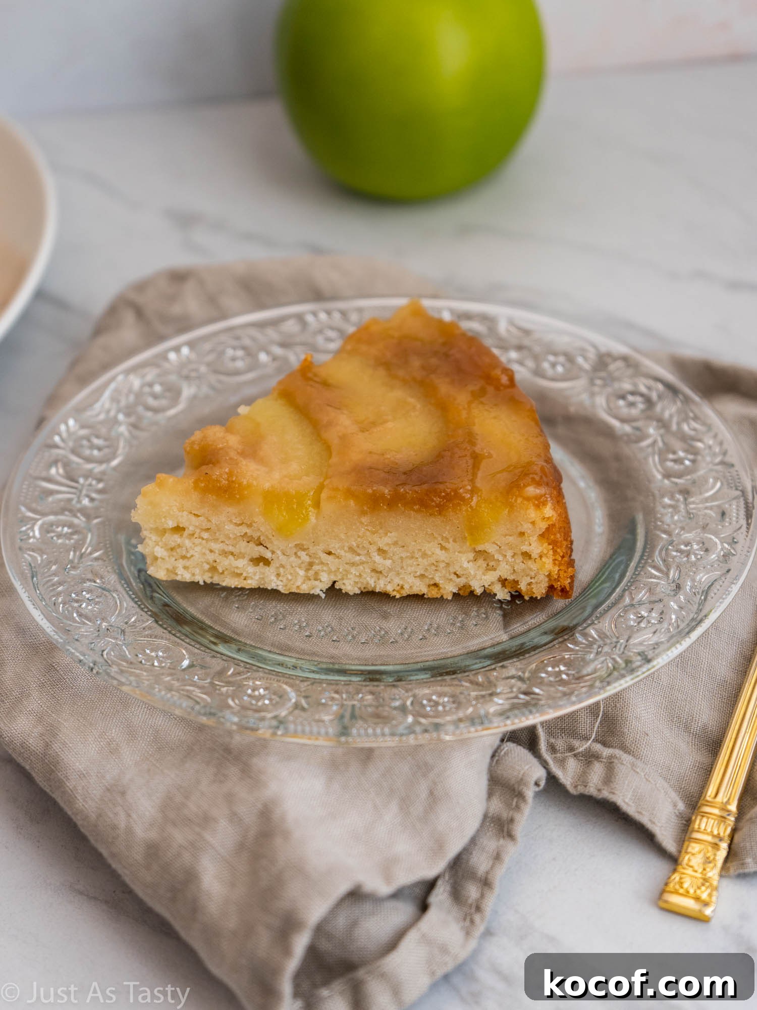 Slice of cake topped with apples on a glass plate.