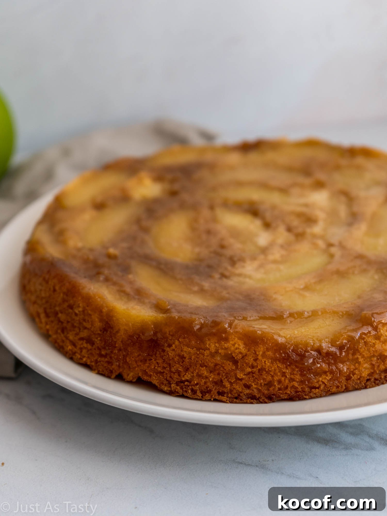 Side view of a round single-layer apple cake on a white plate.