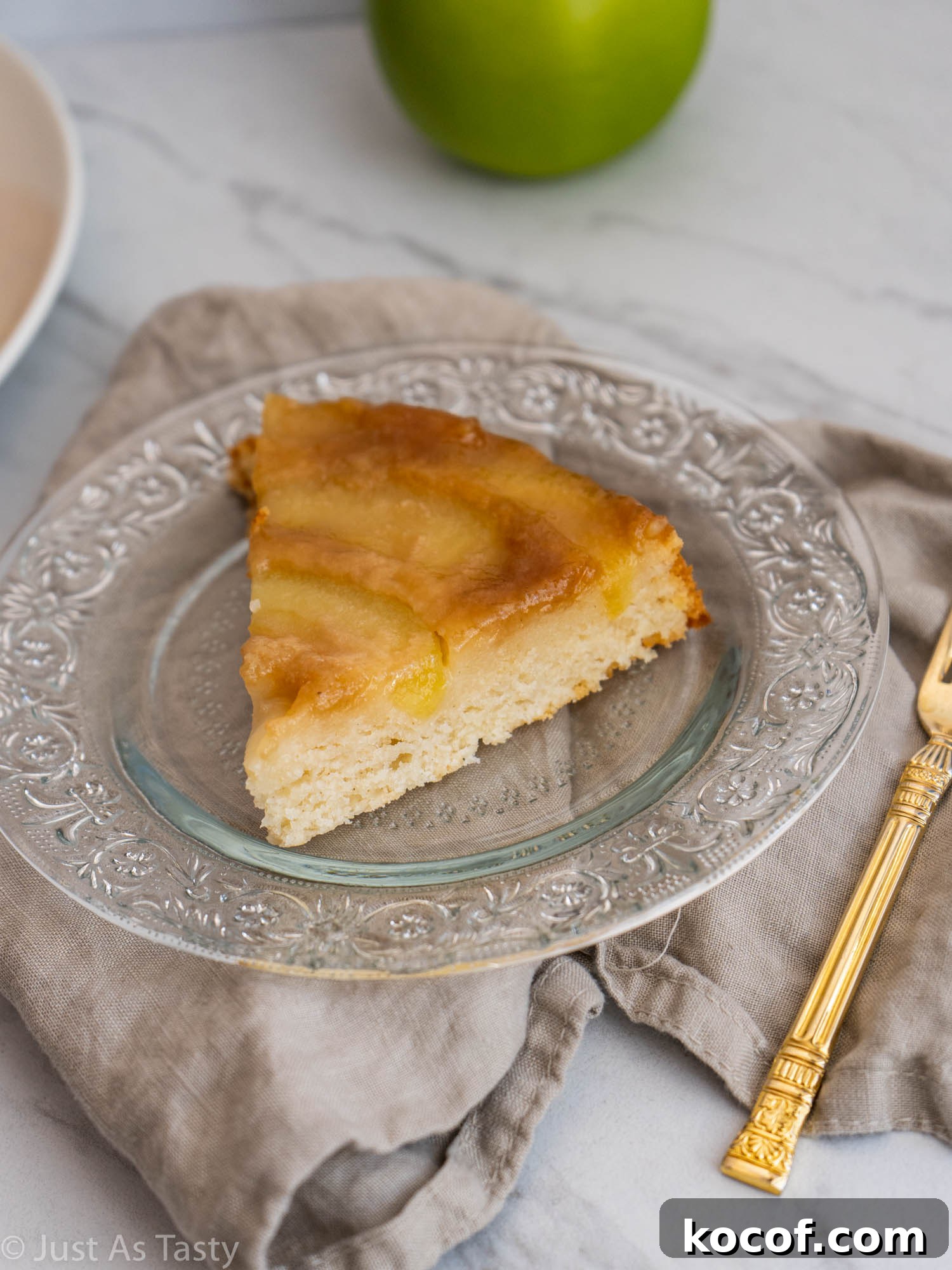 Slice of cake topped with apples on a glass plate.