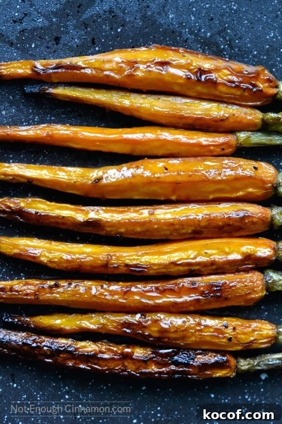 Balsamic-Glazed Roasted Carrots with Honey and Herbs 5 caramelized balsamic roasted carrots lined up horizontally on a dark tabletop