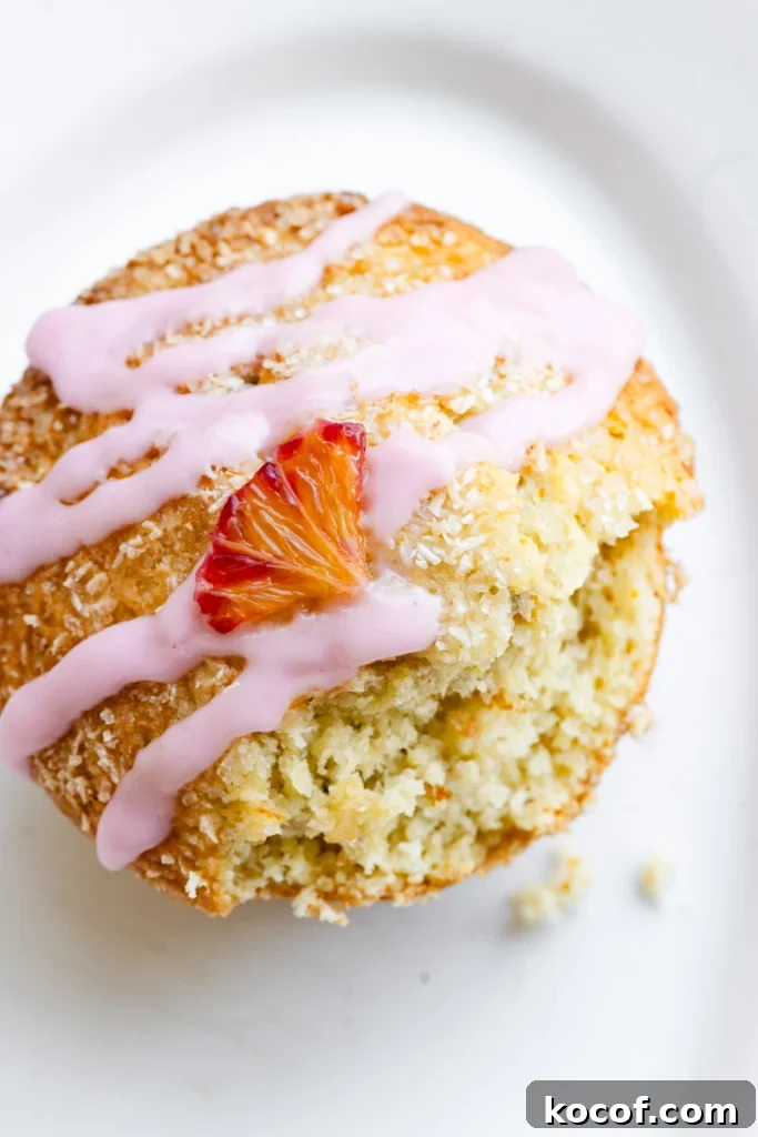 Overhead view of an orange muffin with pink glaze and an orange slice on top of a white plate.