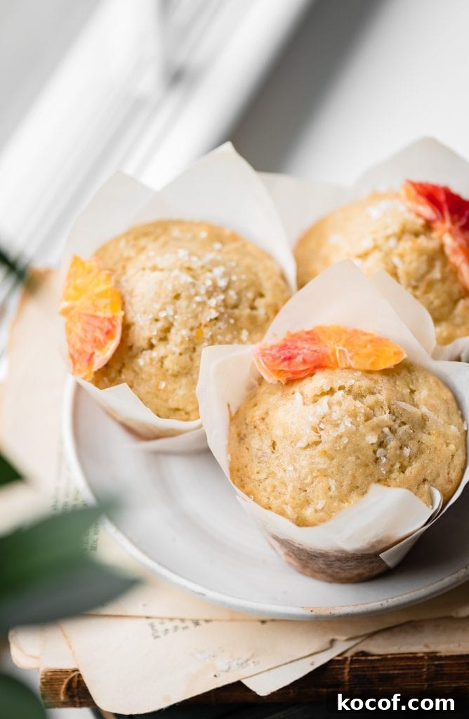 Three orange banana muffins in muffin wrappers on a plate topped with fresh orange slices and coconut.