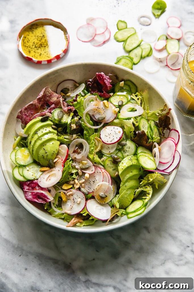 Fresh Garden Salad Recipe: Crisp Mixed Greens & Simple Dressing 3 Top down shot of garden salad in a wide bowl next to sliced onion and cucumber