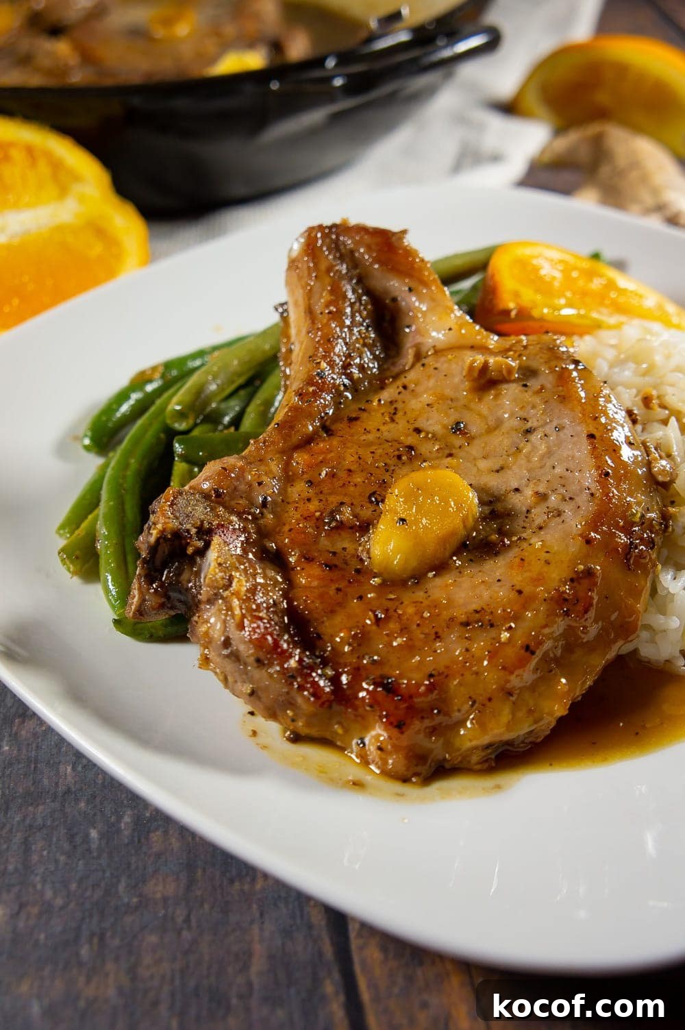a white plate with pork chops, green beans, rice, and a slice of orange