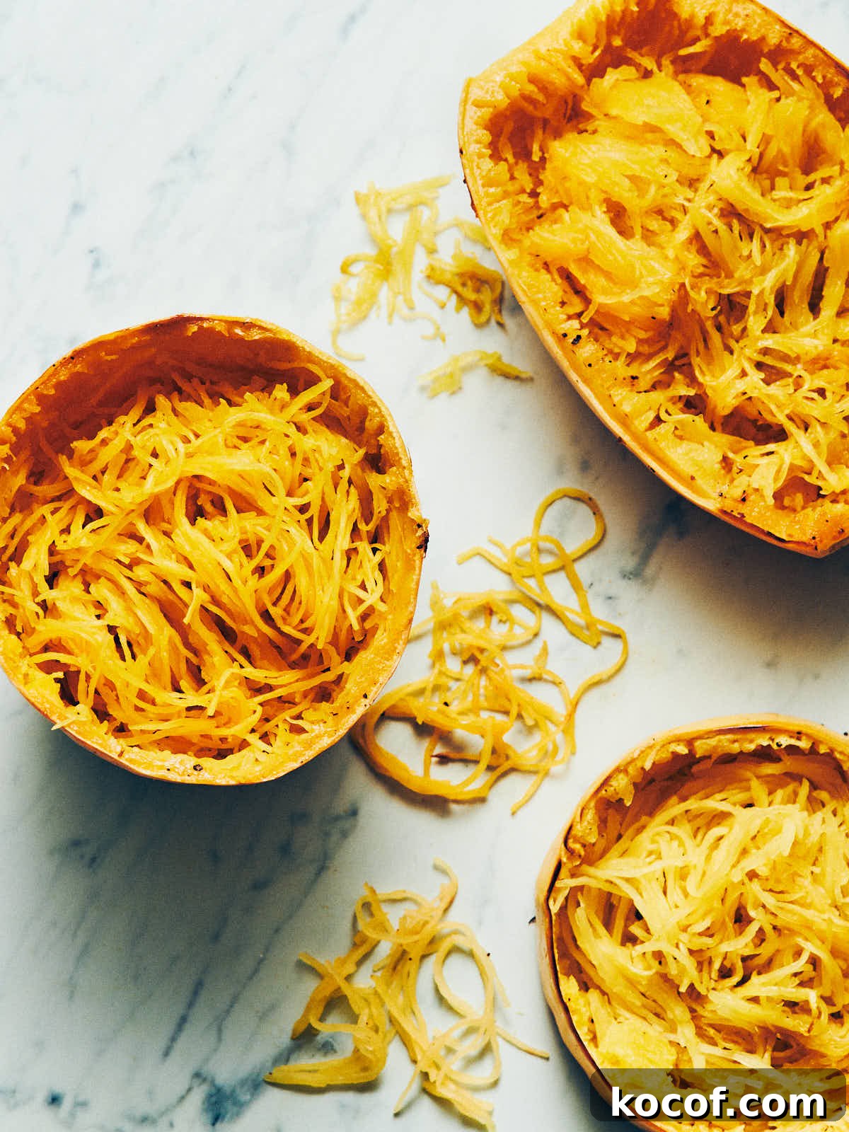 Spaghetti squash cooked three ways with noodles scooped out sitting on a marble surface