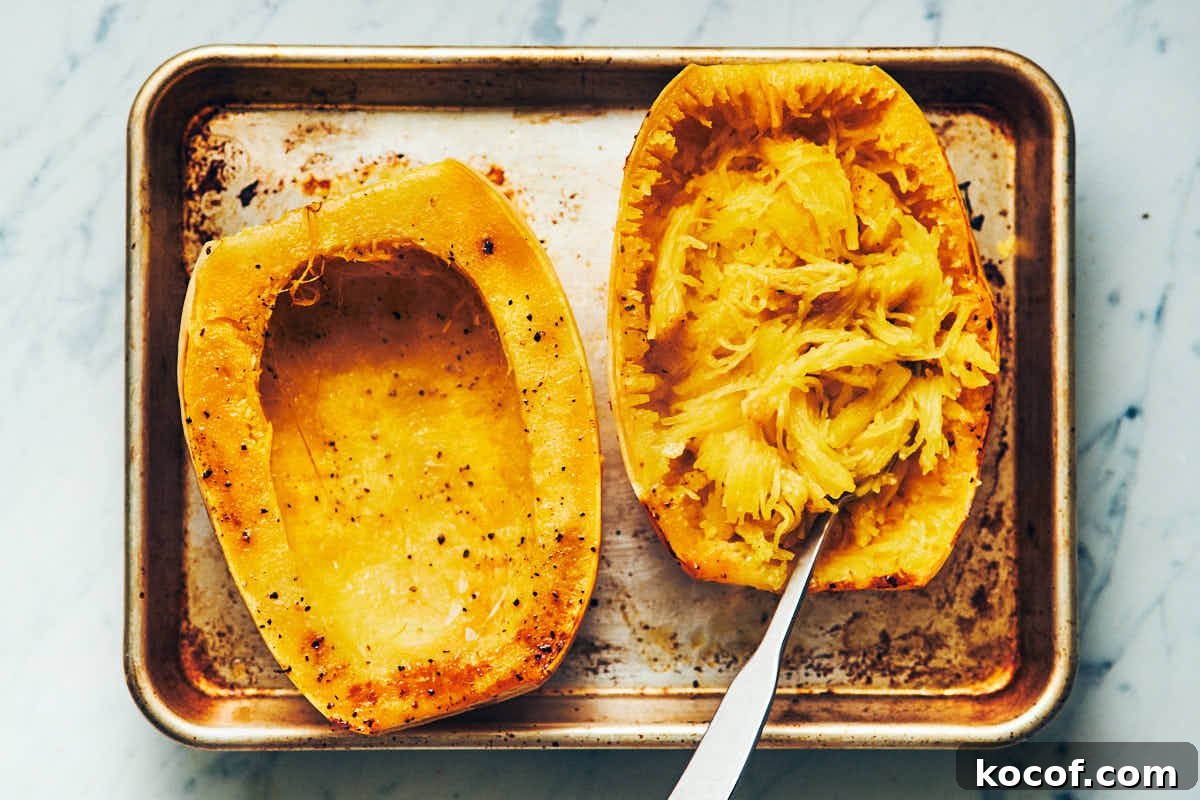 Spaghetti squash cut in half lengthwise and cooked on a metal baking sheet with noodles scooped out