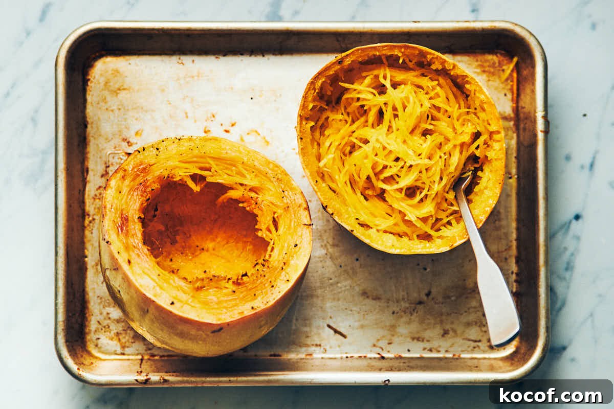 Spaghetti squash cut in half crosswise and cooked on a metal baking sheet with noodles scooped out