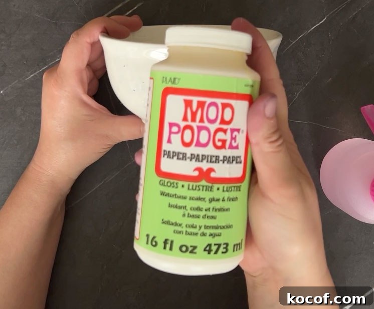 Create a Faux Marble Bowl: Step-by-Step DIY Tutorial 7 Hand holding Mod Podge over a white bowl