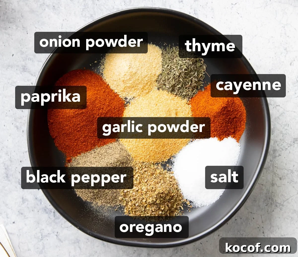 Ingredients for this Cajun Seasoning Recipe sitting in neat piles in a rimmed black dish including smoked paprika, garlic powder, salt, ground black pepper, onion powder, dried oregano, cayenne, and dried thyme.