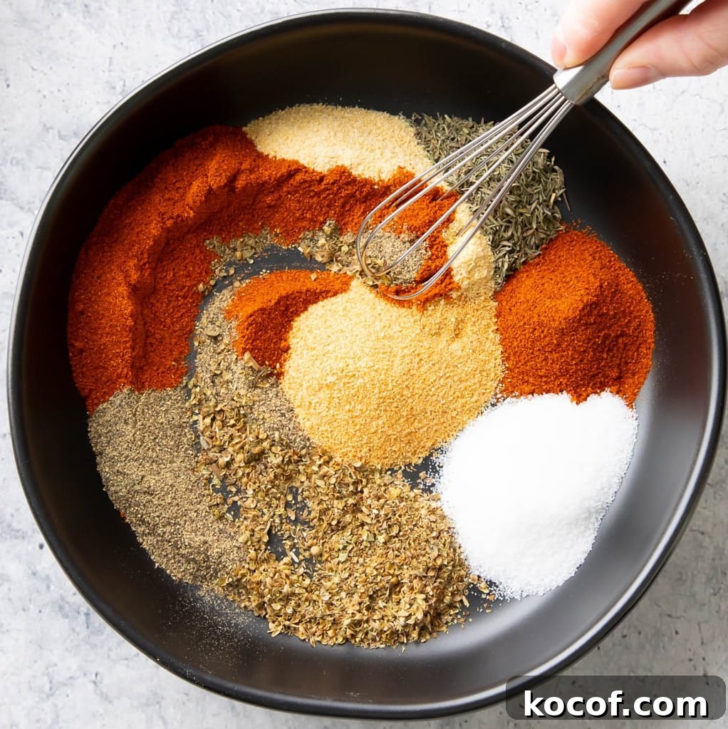 A hand stirring a small whisk into the dish of spices to combine them into Cajun Seasoning