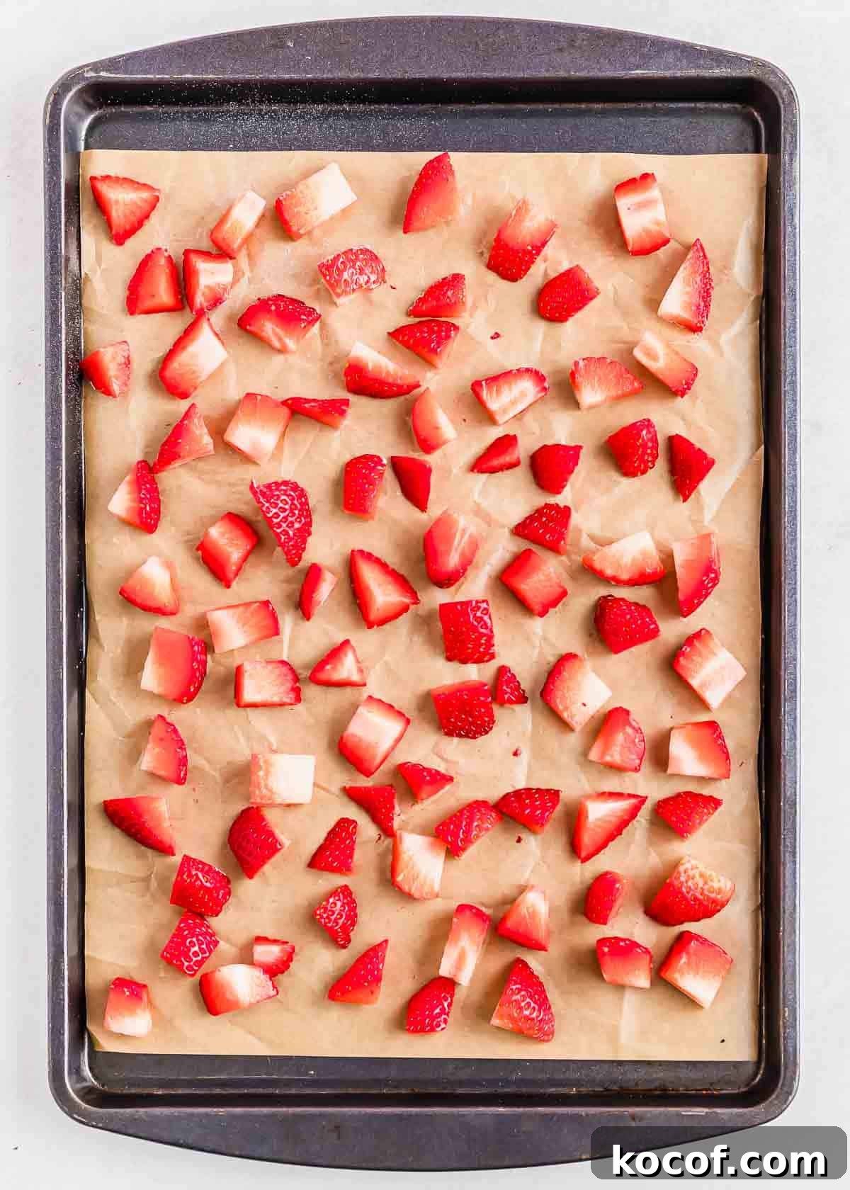 Cubed strawberries are spread evenly across a parchment-lined baking sheet.